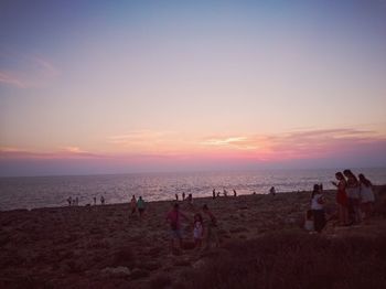 People on beach against sky during sunset