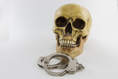 Close-up of human skull and handcuffs against white background