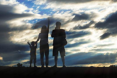 Family standing on field against cloudy sky during sunset