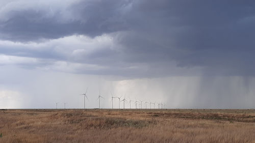 Scenic view wind turbines on field against sky