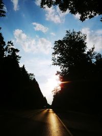 Silhouette trees by road against sky during sunset