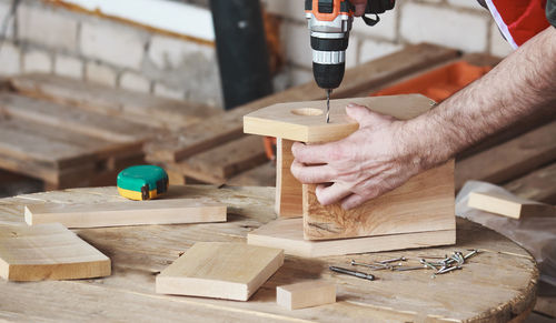 Man collects birdhouse from wooden blanks for birds and screw the screws with cordless screwdriver.