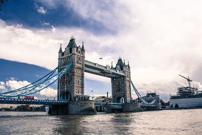 Tower bridge over thames river against cloudy sky