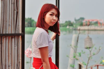 Portrait of beautiful young woman standing against window
