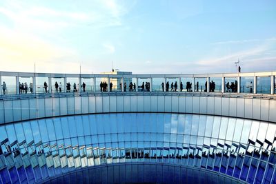 People by railing against blue sky