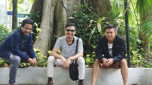 Portrait of friends sitting on plants against trees