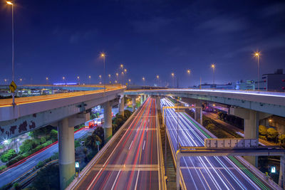 Light trails on bridge in city against sky at night