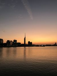 Silhouette buildings by river against sky during sunset