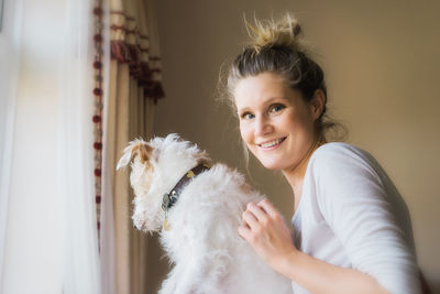 Portrait of woman with jack russell terrier sitting by window at home