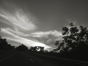 Silhouette trees by road against sky