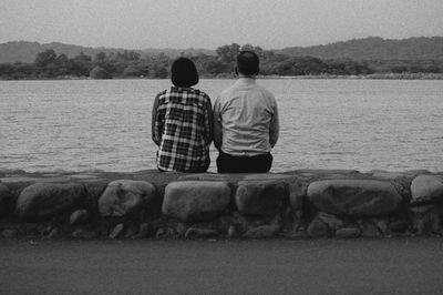Rear view of couple sitting on retaining wall against sea