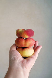 Cropped hand holding stacked fruits against wall