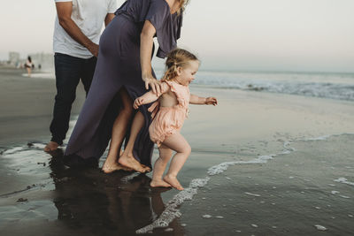 Side view of toddler girl with family running into the ocean at sunset