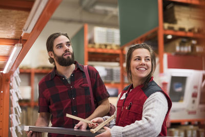 Happy saleswoman looking away while standing with male customer in hardware store