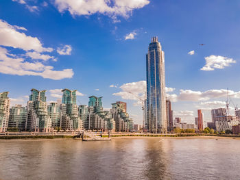 Modern buildings by river against sky in city