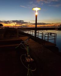 Railing by street light against sky during sunset