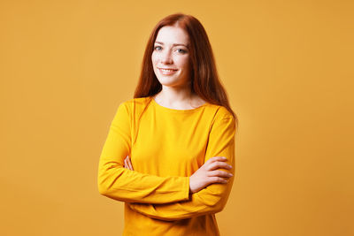 Portrait of young woman standing against yellow background