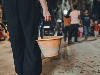 Midsection of woman holding standing with bucket on footpath