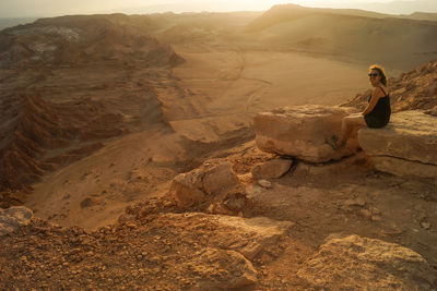 Full length of woman sitting on rock in dessert