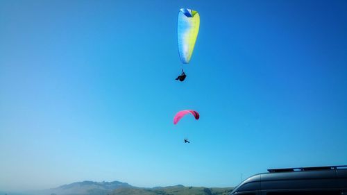 Low angle view of people paragliding against sky