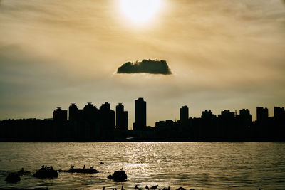 Scenic view of lake by silhouette city against sky during sunset
