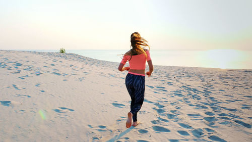 Healthy, young sports beautiful woman runs along the sand, on the beach, in summer, towards the sun
