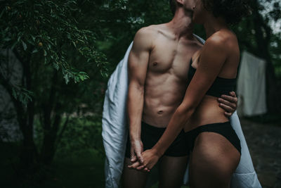 Midsection of shirtless man standing against trees