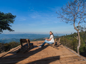 Happy asian woman sit and relax at wooden balcony with mountain view with blue sky at doi chang