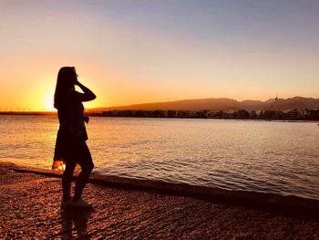 Woman standing on beach against sky during sunset