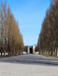 Empty road by trees against blue sky