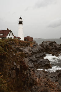 Lighthouse amidst sea and buildings against sky