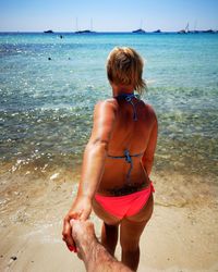 Cropped image of man holding hands with girlfriend standing in bikini at beach