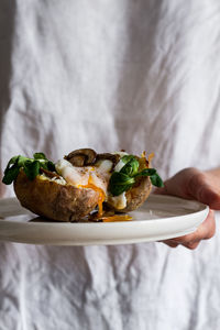 From above of white ceramic bowl with tasty fried egg mushrooms herbs in potato on crop hand