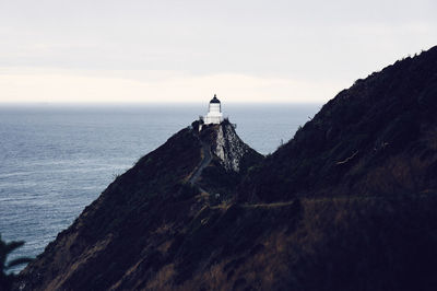 Lighthouse on mountain by sea against sky