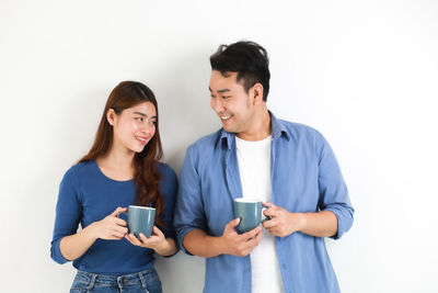 Young couple holding smart phone while standing against white background