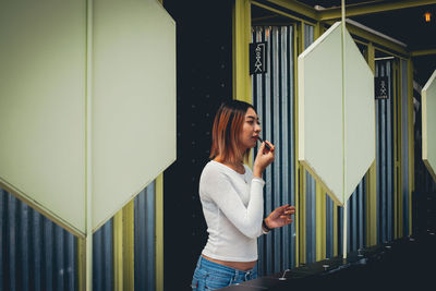 Woman applying lipstick while looking into mirror while standing in bathroom