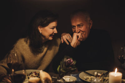 Smiling senior woman talking to mature man with hand on chin at dinner party