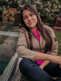 Portrait of young woman sitting by glass window