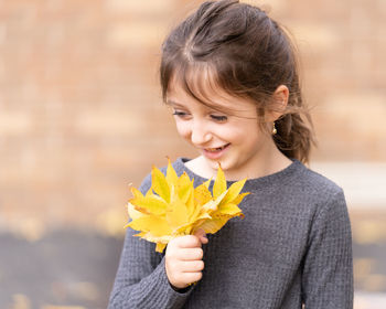 Smiling girl holding leaves while standing outdoors