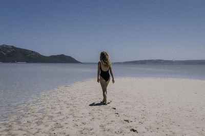 Rear view of woman on beach against clear sky