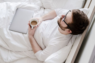 High angle view of man holding coffee cup on bed