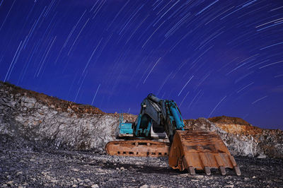 Bulldozer on field against star trails on sky at night