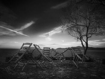 Deck chairs on shore by sea against sky