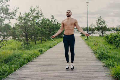 Full length of shirtless man exercising on footpath