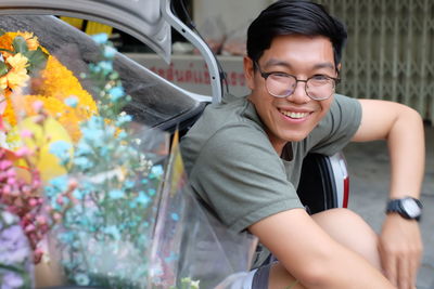 Portrait of smiling young man with bouquet sitting in car trunk