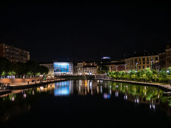 Illuminated buildings by river against sky at night