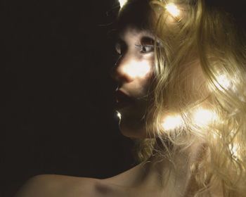 Close-up of woman with illuminated string lights against black background