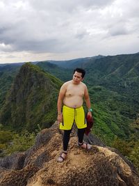 Portrait of young man standing on mountain against sky