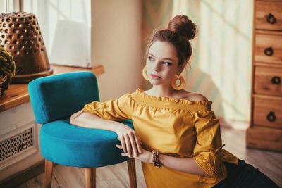 Portrait of young woman sitting on chair at home