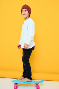 Portrait of young woman standing against yellow background